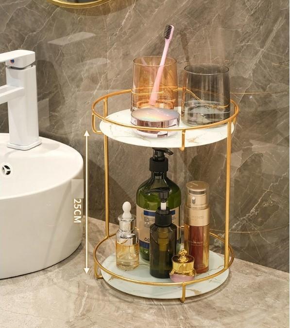 Gold two-tier bathroom countertop organizer with white marble-style shelves holding toiletries and cosmetics