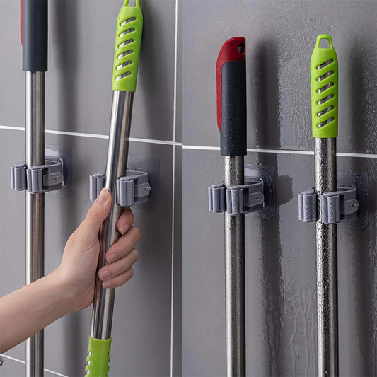 Self-adhesive mop and broom holders mounted on a tiled wall holding cleaning handles
