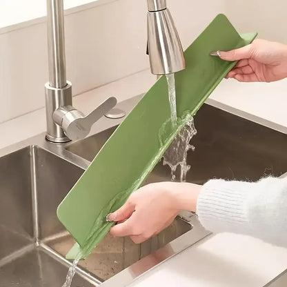 Flexible green silicone sink splash guard with suction cups being rinsed under a kitchen faucet